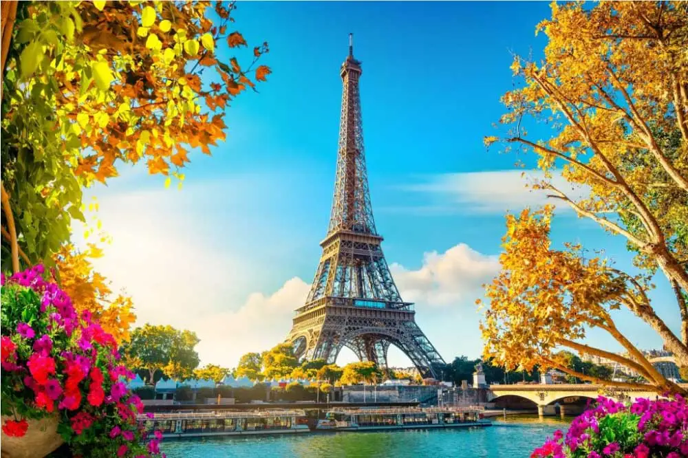 A Torre Eiffel vista através de árvores coloridas em Paris, com o rio Sena em primeiro plano.