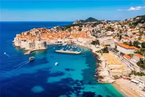 Praia e cidade antiga de Dubrovnik, na Croácia, com vista do mar azul e muralhas medievais.