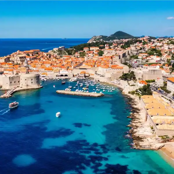 Praia e cidade antiga de Dubrovnik, na Croácia, com vista do mar azul e muralhas medievais.
