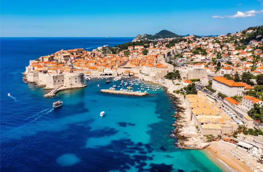 Praia e cidade antiga de Dubrovnik, na Croácia, com vista do mar azul e muralhas medievais.