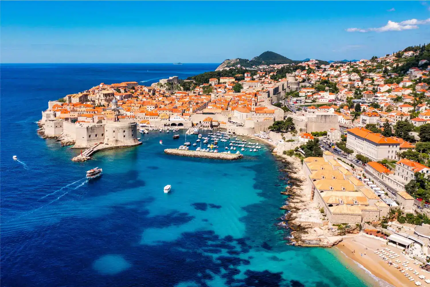 Praia e cidade antiga de Dubrovnik, na Croácia, com vista do mar azul e muralhas medievais.