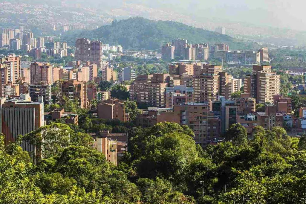 Uma paisagem urbana com edifícios altos em meio a uma vegetação exuberante, com uma montanha ao fundo.