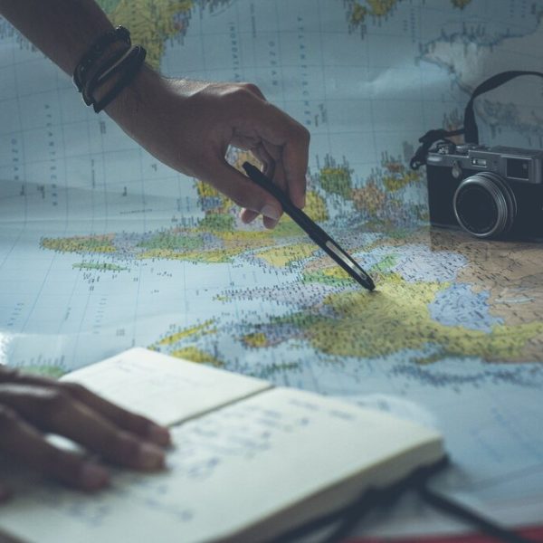 Visão de cima de uma pessoa planejando uma viagem com um mapa, um notebook, uma caneta e uma câmera vintage.