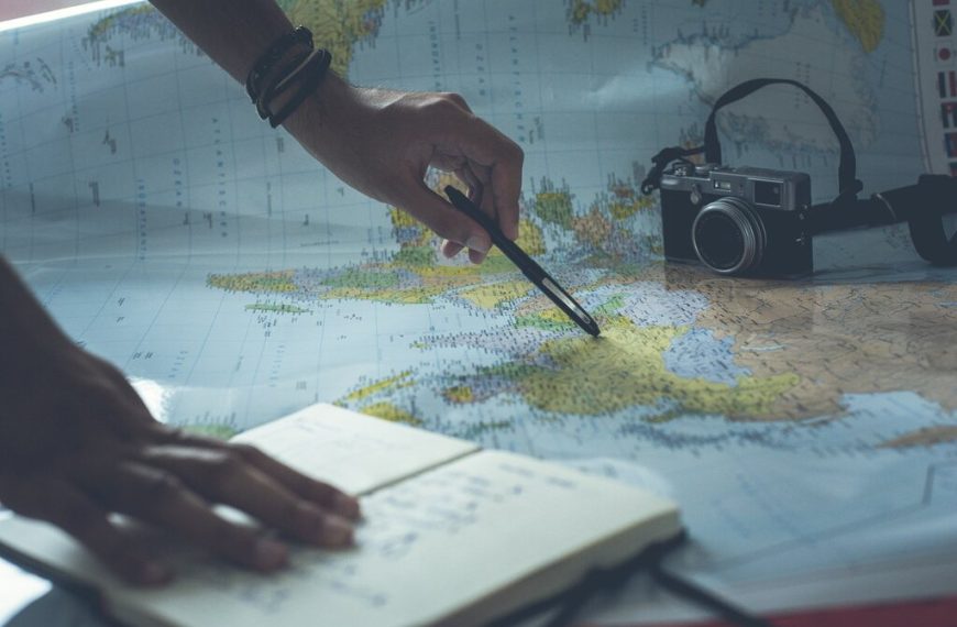 Visão de cima de uma pessoa planejando uma viagem com um mapa, um notebook, uma caneta e uma câmera vintage.