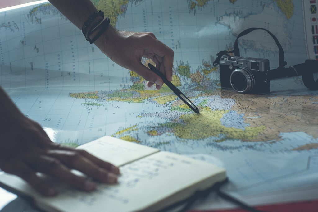 Visão de cima de uma pessoa planejando uma viagem com um mapa, um notebook, uma caneta e uma câmera vintage.