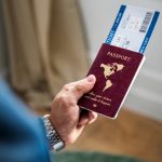 Uma mão segurando um passaporte vermelho e uma passagem aérea.