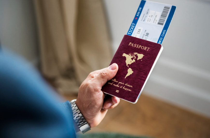 Uma mão segurando um passaporte vermelho e uma passagem aérea.
