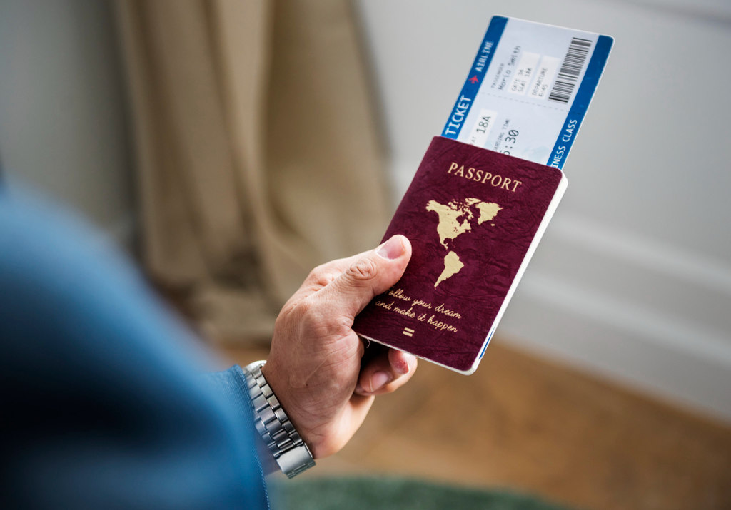 Uma mão segurando um passaporte vermelho e uma passagem aérea.