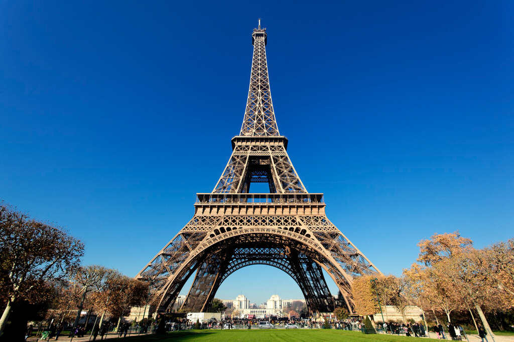 Fotografia da Torre Eiffel a partir do solo, mostrando sua estrutura de treliça de ferro intrincada com o céu azul vívido ao fundo.