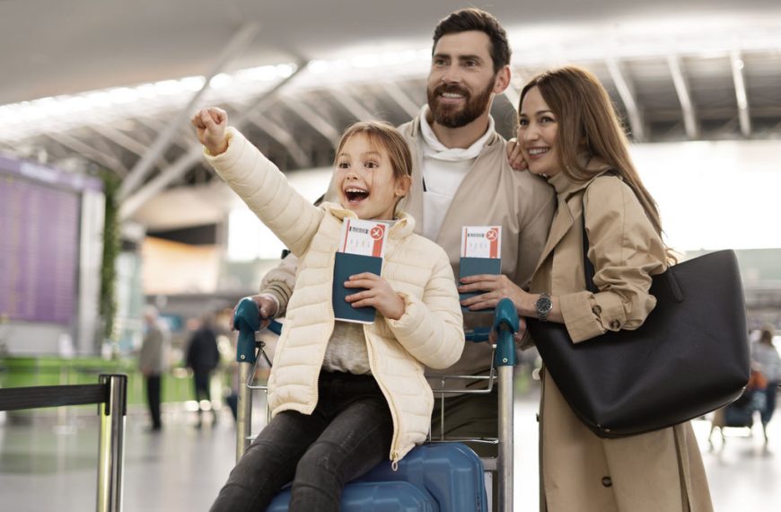 Família de três pessoas felizes no aeroporto, com a criança segurando passagens, todos sorrindo e comemorando a viagem.