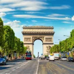 O Arco do Triunfo em Paris, visto de uma rua movimentada alinhada com árvores.