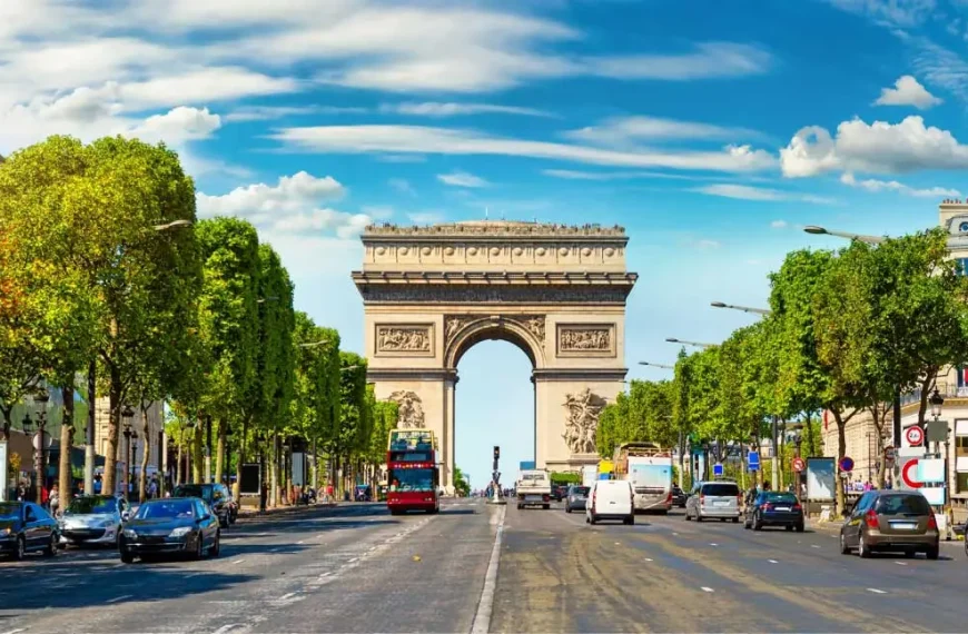 O Arco do Triunfo em Paris, visto de uma rua movimentada alinhada com árvores.