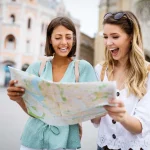 Imagem mostrando duas turistas planejando seu itinerário de viagem com um mapa, exibindo felicidade e antecipação.