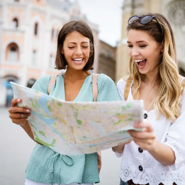Imagem mostrando duas turistas planejando seu itinerário de viagem com um mapa, exibindo felicidade e antecipação.