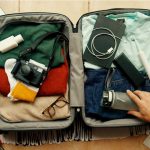 uma mão arrumando a mala para viagem em cima de uma mesa com produtos tecnológicos.