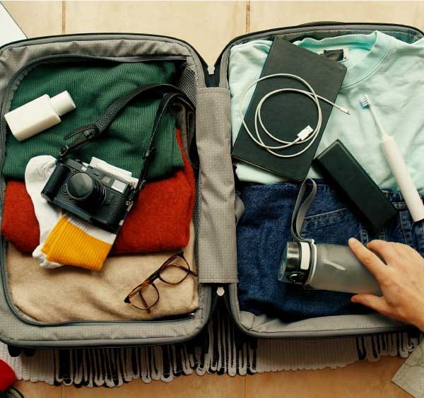 uma mão arrumando a mala para viagem em cima de uma mesa com produtos tecnológicos.