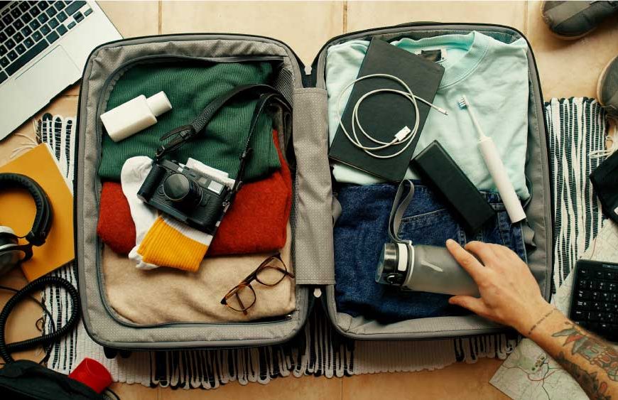 uma mão arrumando a mala para viagem em cima de uma mesa com produtos tecnológicos.