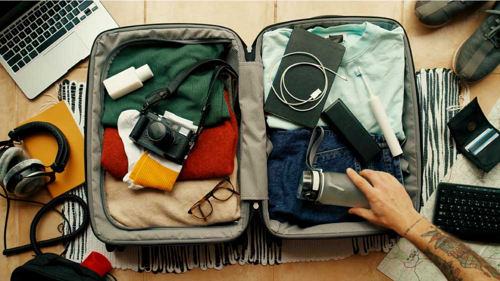 uma mão arrumando a mala para viagem em cima de uma mesa com produtos tecnológicos.