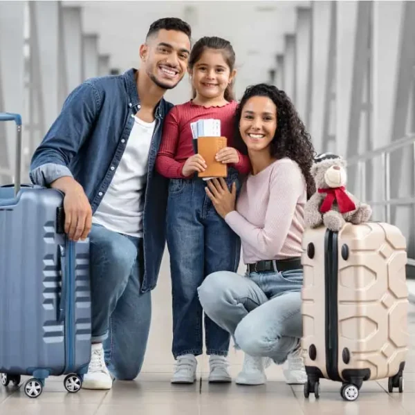 Família de três posando com bagagem em um terminal de aeroporto. A filha está segurando um passaporte e um bilhete.