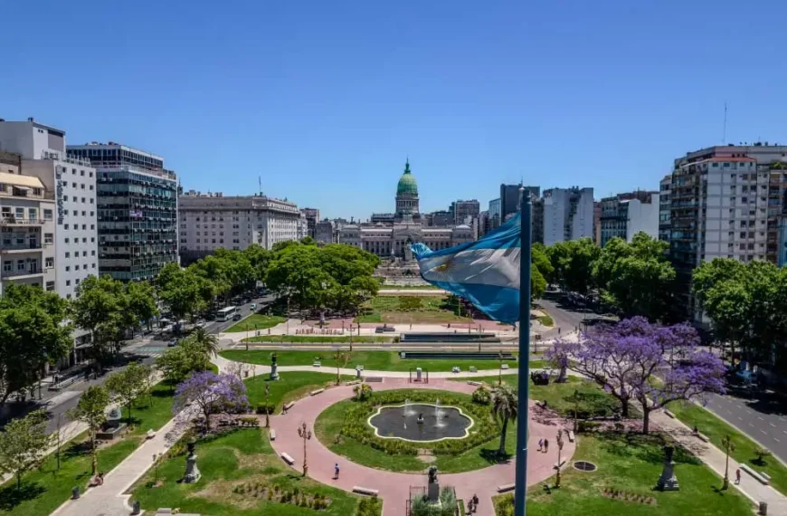 Bandeira argentina esvoaçando com o prédio do Congresso Nacional e um parque paisagístico ao fundo em Buenos Aires, Argentina. A cena é vista de cima e mostra edifícios circundantes.
