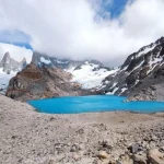 Imagem de um lago de cor azul vibrante cercado por montanhas rochosas e cobertas de neve