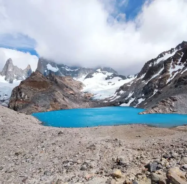 Imagem de um lago de cor azul vibrante cercado por montanhas rochosas e cobertas de neve