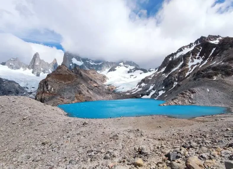 Imagem de um lago de cor azul vibrante cercado por montanhas rochosas e cobertas de neve
