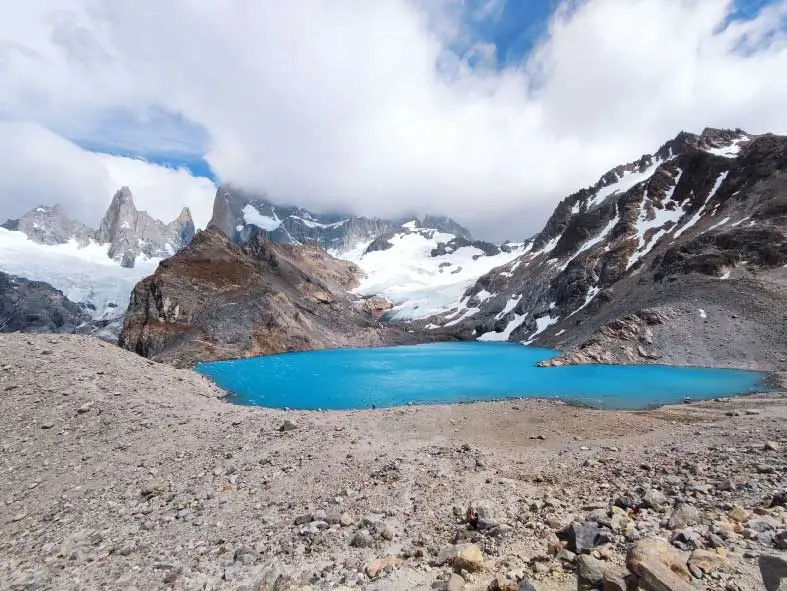 Imagem de um lago de cor azul vibrante cercado por montanhas rochosas e cobertas de neve
