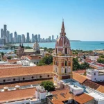 Uma vista aérea de Cartagena, Colômbia, com telhados de terracota, uma torre da igreja e arranha-céus modernos ao fundo.