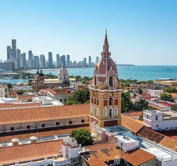 Uma vista aérea de Cartagena, Colômbia, com telhados de terracota, uma torre da igreja e arranha-céus modernos ao fundo.