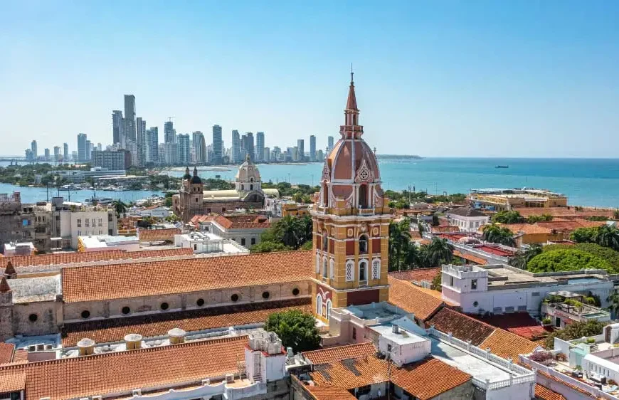 Uma vista aérea de Cartagena, Colômbia, com telhados de terracota, uma torre da igreja e arranha-céus modernos ao fundo.