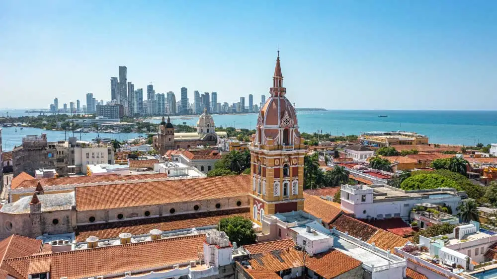 Uma vista aérea de Cartagena, Colômbia, com telhados de terracota, uma torre da igreja e arranha-céus modernos ao fundo.