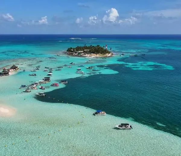 Vista aérea de ilha e bancos de areia em águas turquesa com vários barcos ancorados.