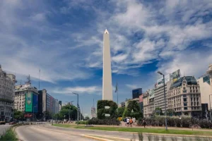 Imagem da praça do obelisco em Buenos Aires, com arbustos bem cuidados formando figuras geométricas, e prédios históricos ao redor.