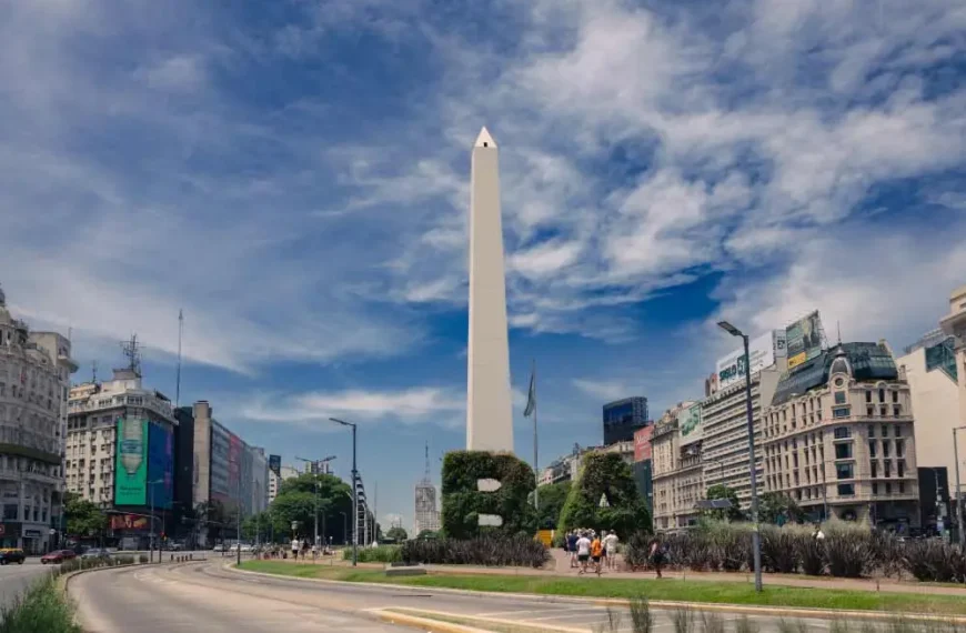 Imagem da praça do obelisco em Buenos Aires, com arbustos bem cuidados formando figuras geométricas, e prédios históricos ao redor.