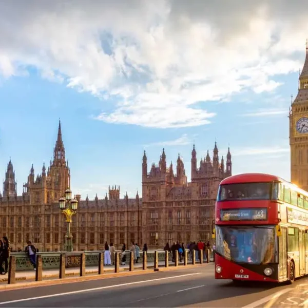 Imagem de um ônibus de dois andares vermelho e verde no lado de uma ponte na cidade de Londres, com o Big Ben e o Palácio de Westminster ao fundo.