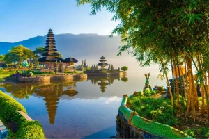 Templo Pura Ulun Danu Bratan em Bali, Indonésia, às margens do lago Bratan, com pagodes hindus refletidos na água, montanhas ao fundo, vegetação tropical e paisagem exótica ao amanhecer.