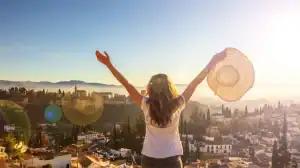 Mulher com chapéu aproveitando o pôr do sol na cidade, simbolizando liberdade e bem-estar.