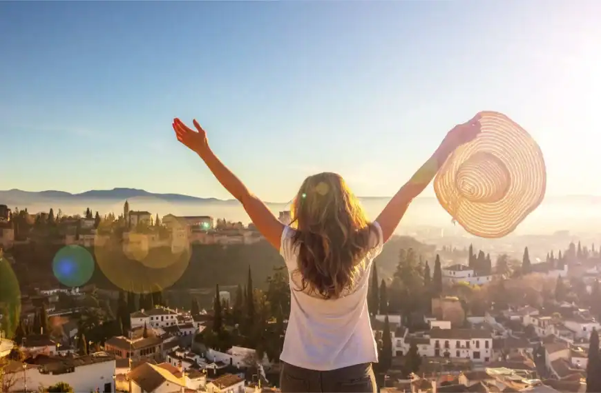 Mulher com chapéu aproveitando o pôr do sol na cidade, simbolizando liberdade e bem-estar.
