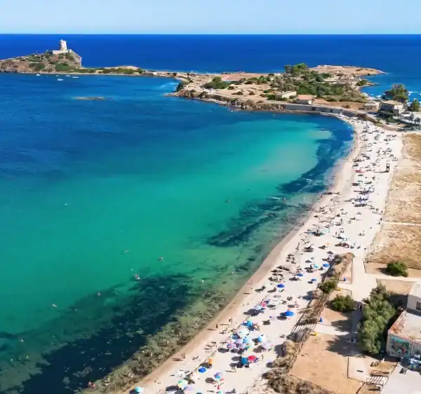 Vista aérea de uma praia de águas cristalinas em tons de azul-turquesa e verde, com faixa de areia cheia de banhistas e guarda-sóis. Ao fundo, pequenas ilhas rochosas conectadas por uma estreita faixa de terra e o mar azul intenso se estendendo até o horizonte sob céu limpo.