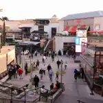 Área de lazer com lojas, restaurantes e pessoas caminhando ao ar livre.