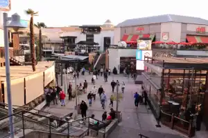 Área de lazer com lojas, restaurantes e pessoas caminhando ao ar livre.