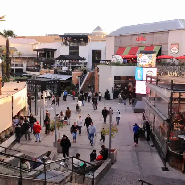 Área de lazer com lojas, restaurantes e pessoas caminhando ao ar livre.