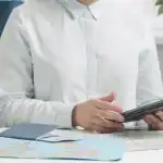 Imagem de uma pessoa segurando um tablet, com mapas e documentos de viagem sobre a mesa, simbolizand.