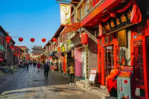 Rua comercial tradicional decorada com lanternas vermelhas chinesas, cercada por lojas, restaurantes e edifícios históricos, com pedestres caminhando em um bairro cultural durante o dia
