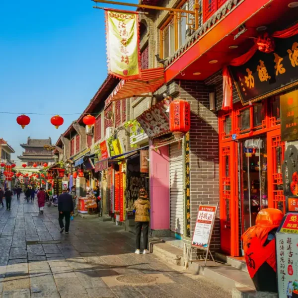 Rua comercial tradicional decorada com lanternas vermelhas chinesas, cercada por lojas, restaurantes e edifícios históricos, com pedestres caminhando em um bairro cultural durante o dia