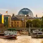 "Um barco navegando no rio Spree, em Berlim, durante o entardecer, com o edifício do Reichstag e sua icônica cúpula de vidro ao fundo."