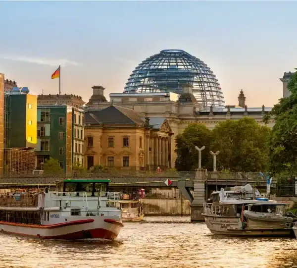 "Um barco navegando no rio Spree, em Berlim, durante o entardecer, com o edifício do Reichstag e sua icônica cúpula de vidro ao fundo."