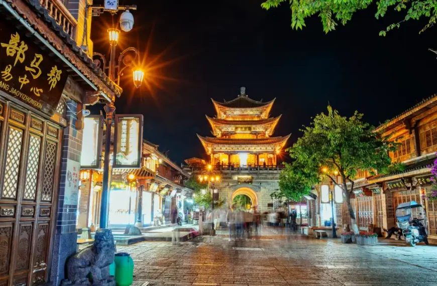Rua histórica na China à noite, com arquitetura tradicional chinesa, lojas iluminadas por lanternas e um imponente pagode dourado ao fundo, cercado por árvores e construções típicas.